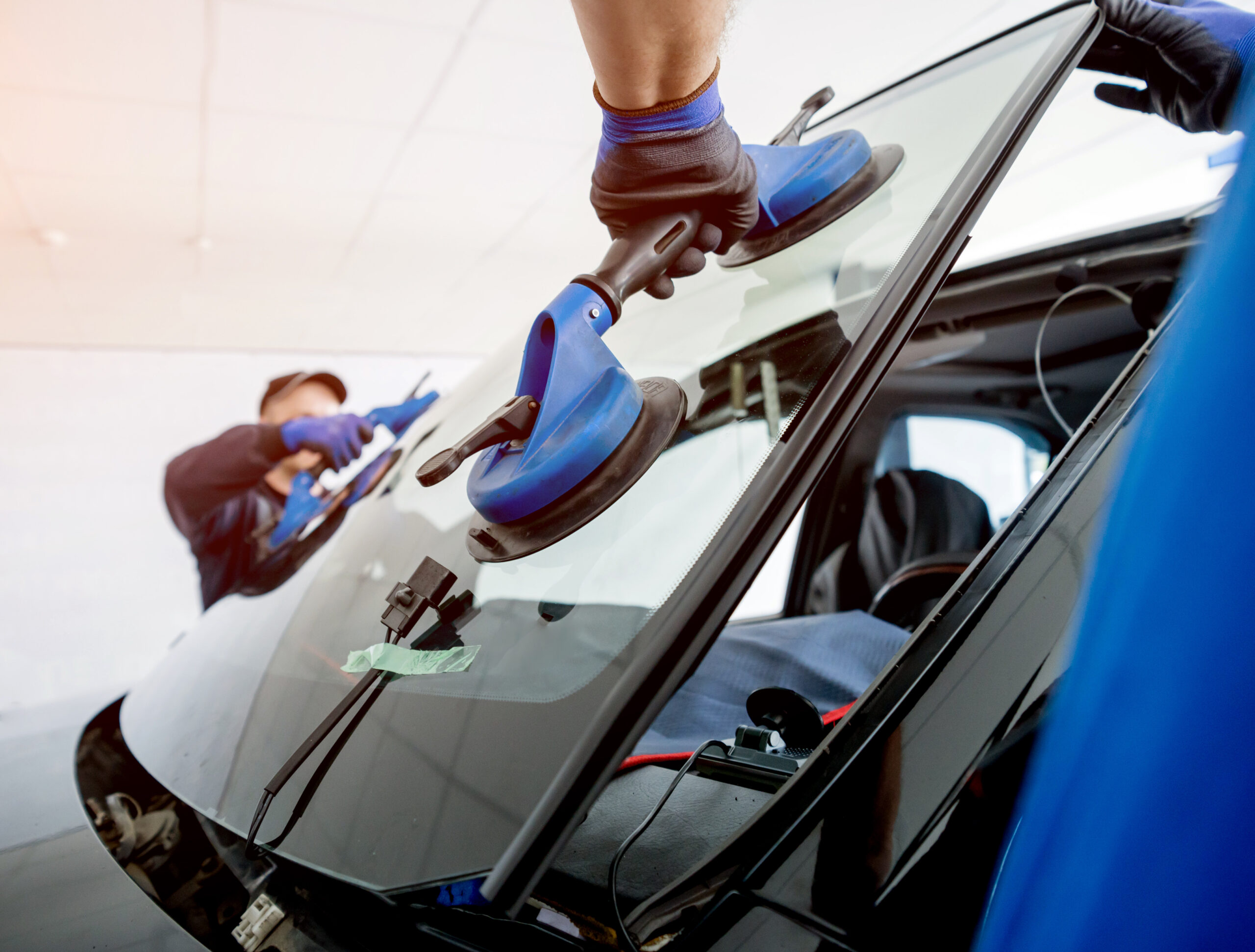 Automobile special workers replacing windscreen or windshield of a car in auto service station garage. Background